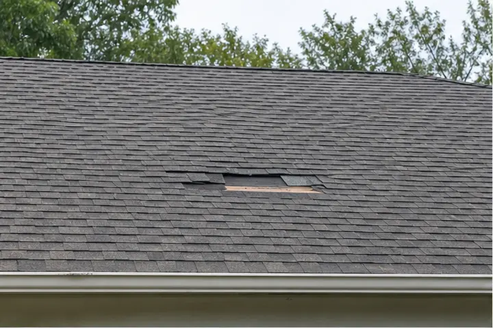 Asphalt shingle roof with damaged and missing shingle patches.
